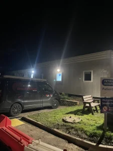 A night view showing the front of Tetbury Hospital with Stroud Electrical Services vans parked near the entrance.