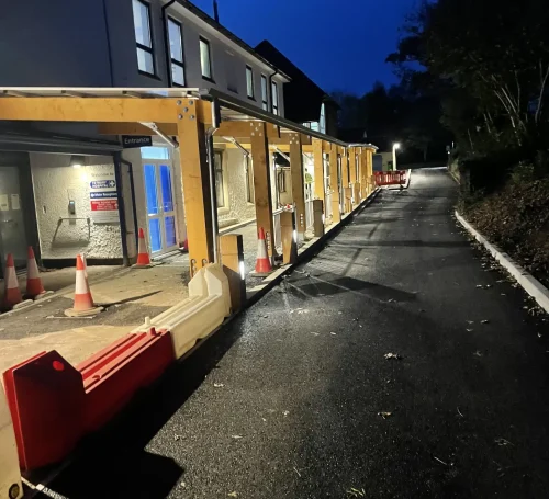 Nighttime view of a newly constructed or renovated walkway with lighting, leading up to a modern-looking building entrance.